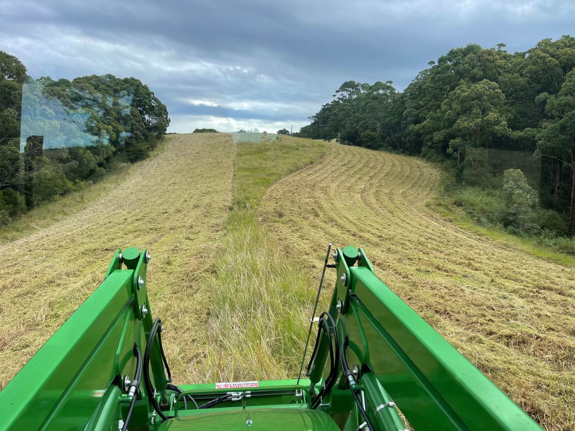 Green Tractor Driving Through a Field, Trees on the Sides, Cloudy Sky — Coastal Slashing & Mowing Services In Tallwoods Village, NSW
