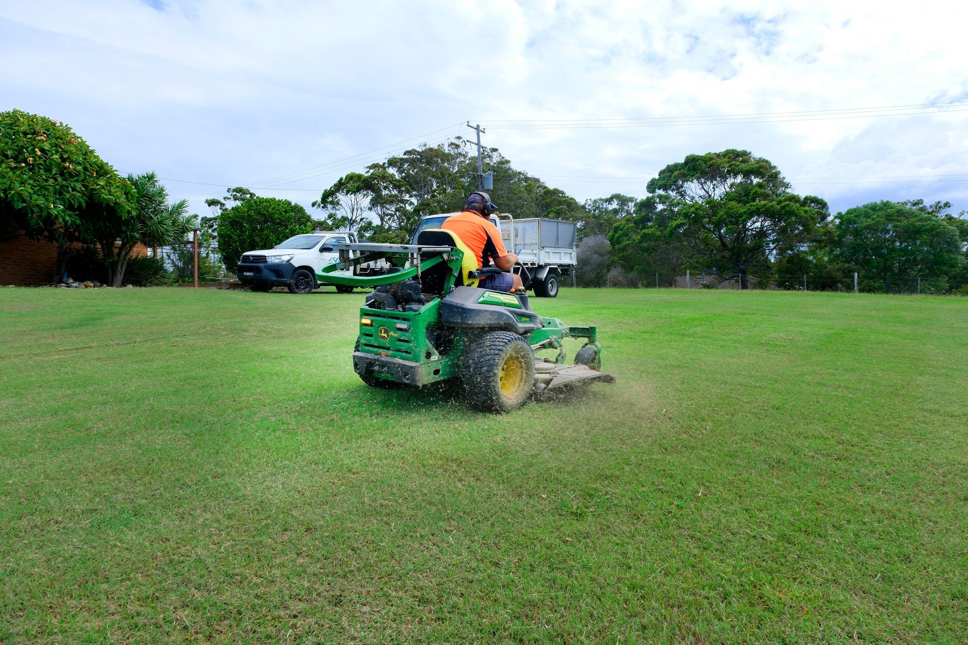 Two Tractors and a White Truck on a Grassy Field; One Tractor Has a Mower — Coastal Slashing & Mowing Services In Tallwoods Village, NSW