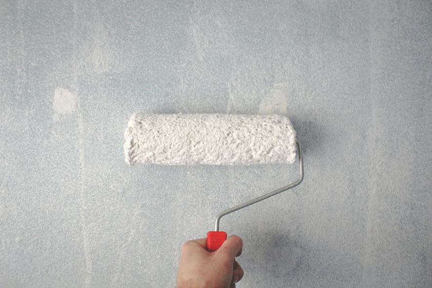 Hand rolling white paint onto a light blue wall with a red handled roller.