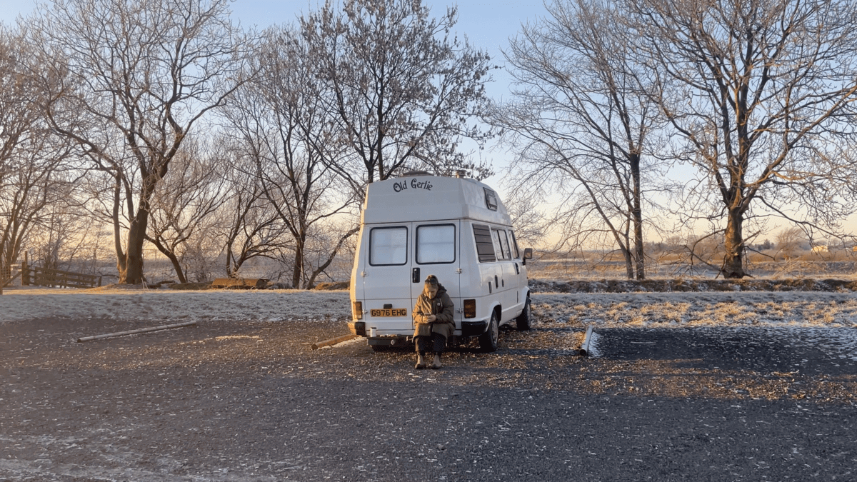 Kez and Old Gertie parked in a car park with trees in the background.