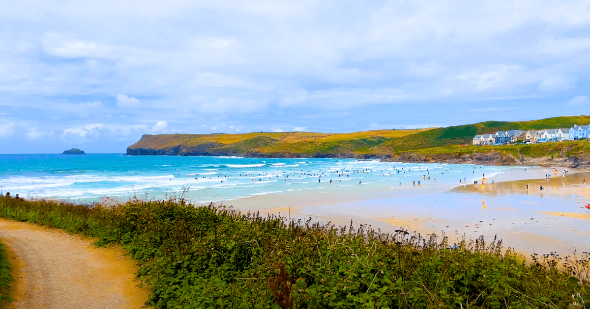A path leading to a beach with people swimming in the ocean.