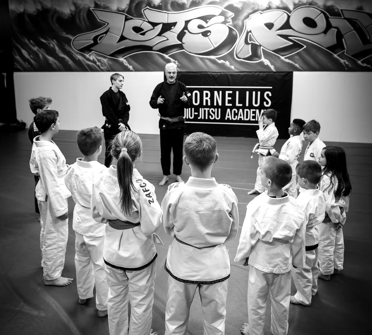 A group of children are standing in a circle in front of a sign that says cornelius ju-jitsu academy