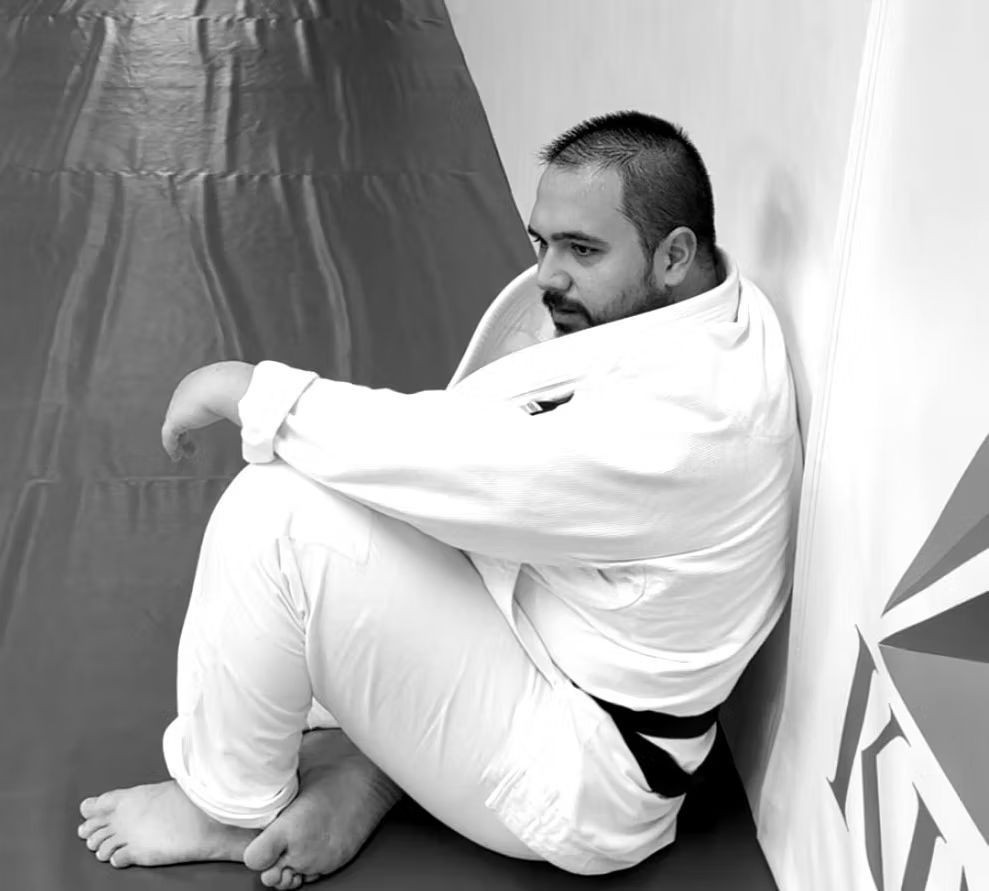 A man in a Gi sits on the floor leaning against a wall