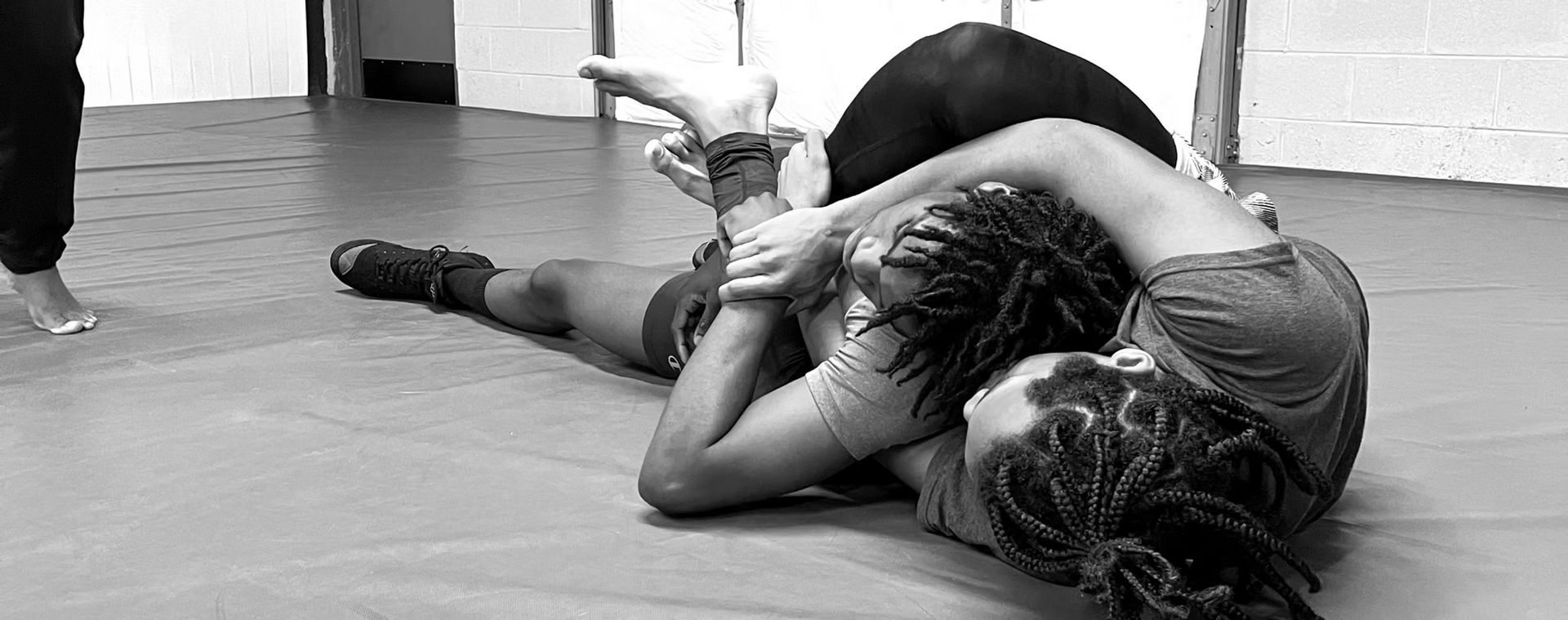 Two women are wrestling on a mat in a gym.
