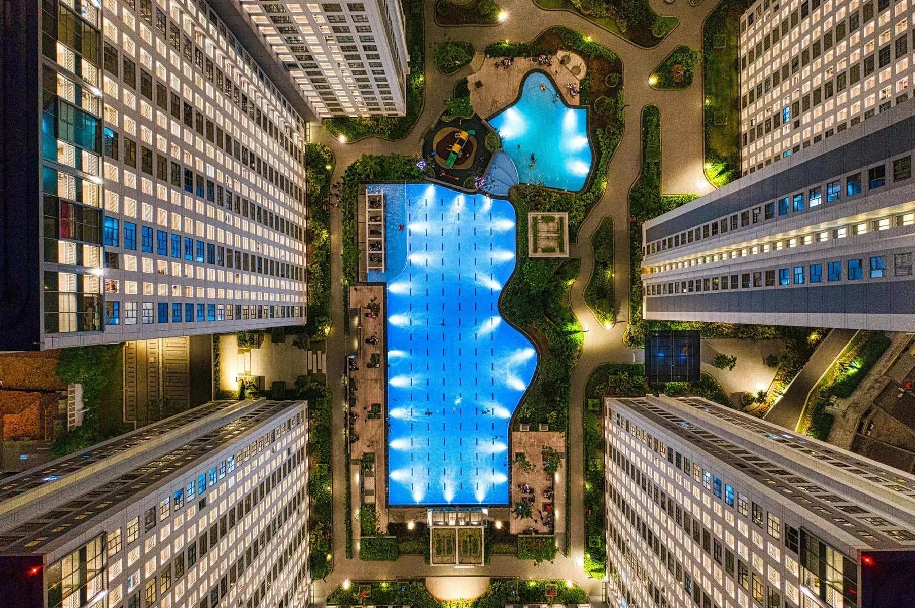 Overhead view of illuminated swimming pools surrounded by tall apartment buildings.