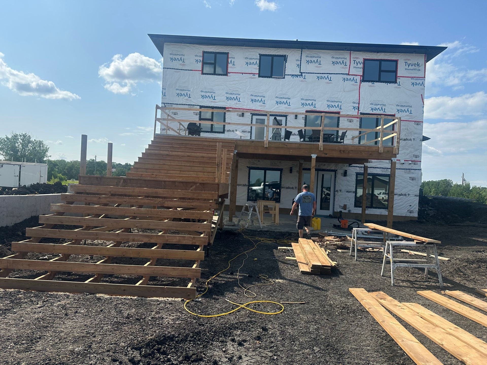 Two workers installing green siding on a house exterior, ladders on either side, sunny day.