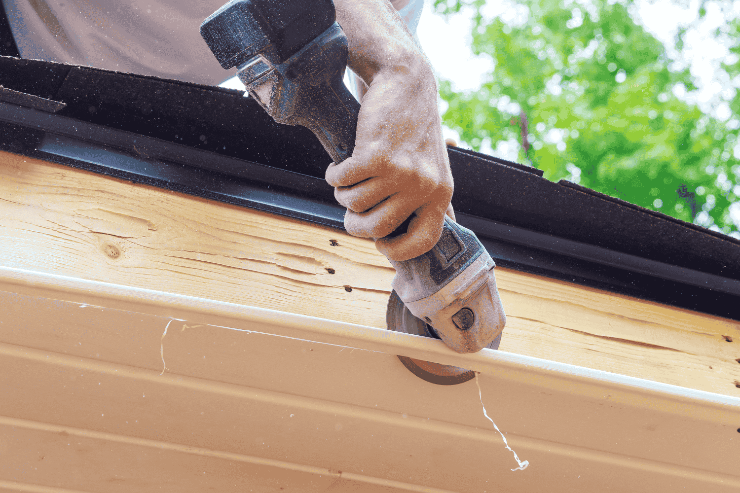Person using a power saw to cut a white gutter on a building's edge.