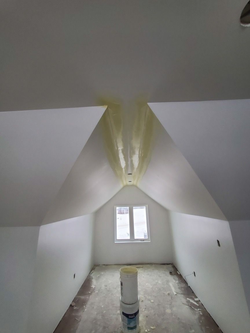 Bedroom with slanted ceiling, bed with white bedding, small window with curtains, and luggage rack.