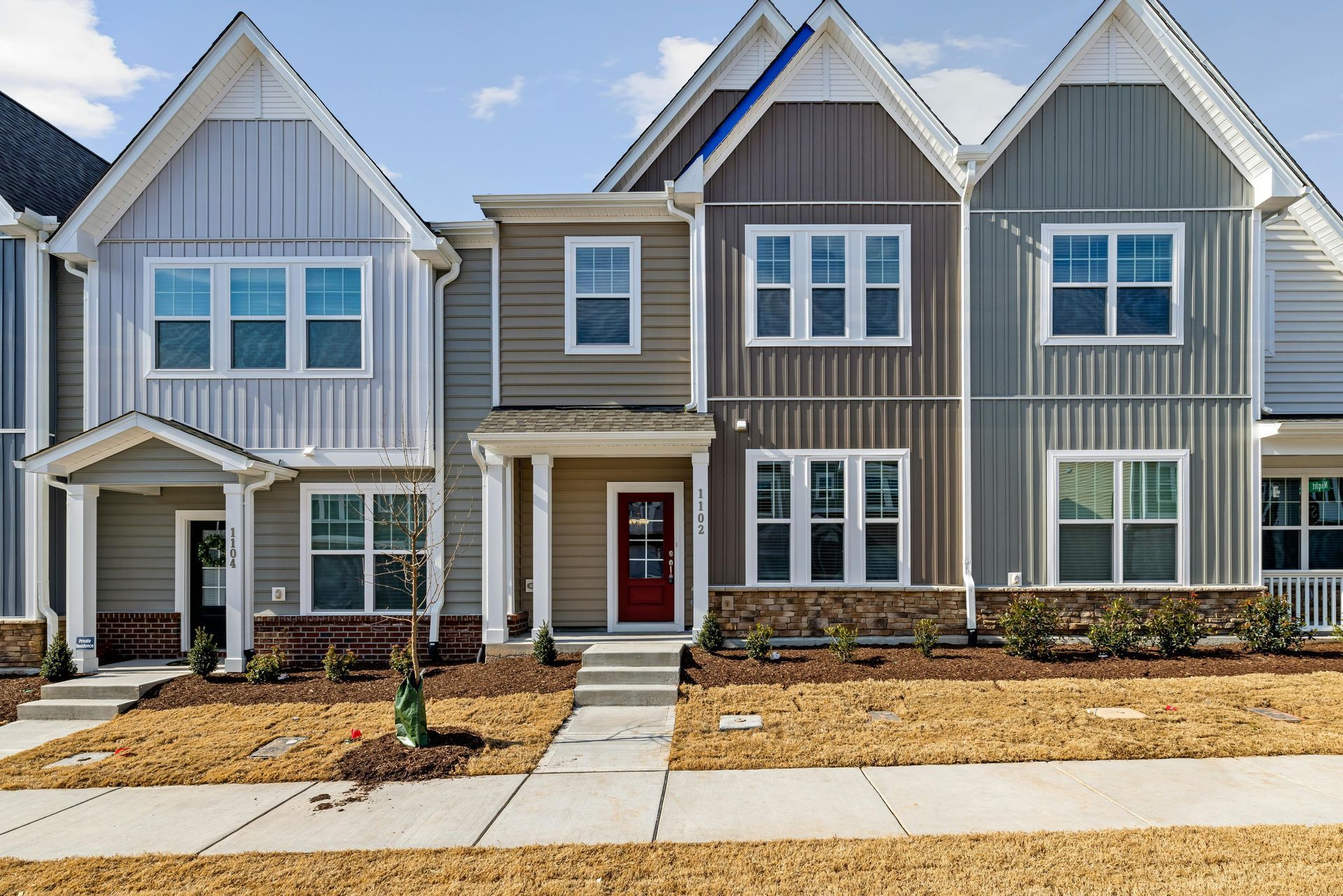 Row of new townhomes with varying gray, brown, and blue siding, each with a front porch and walkway.