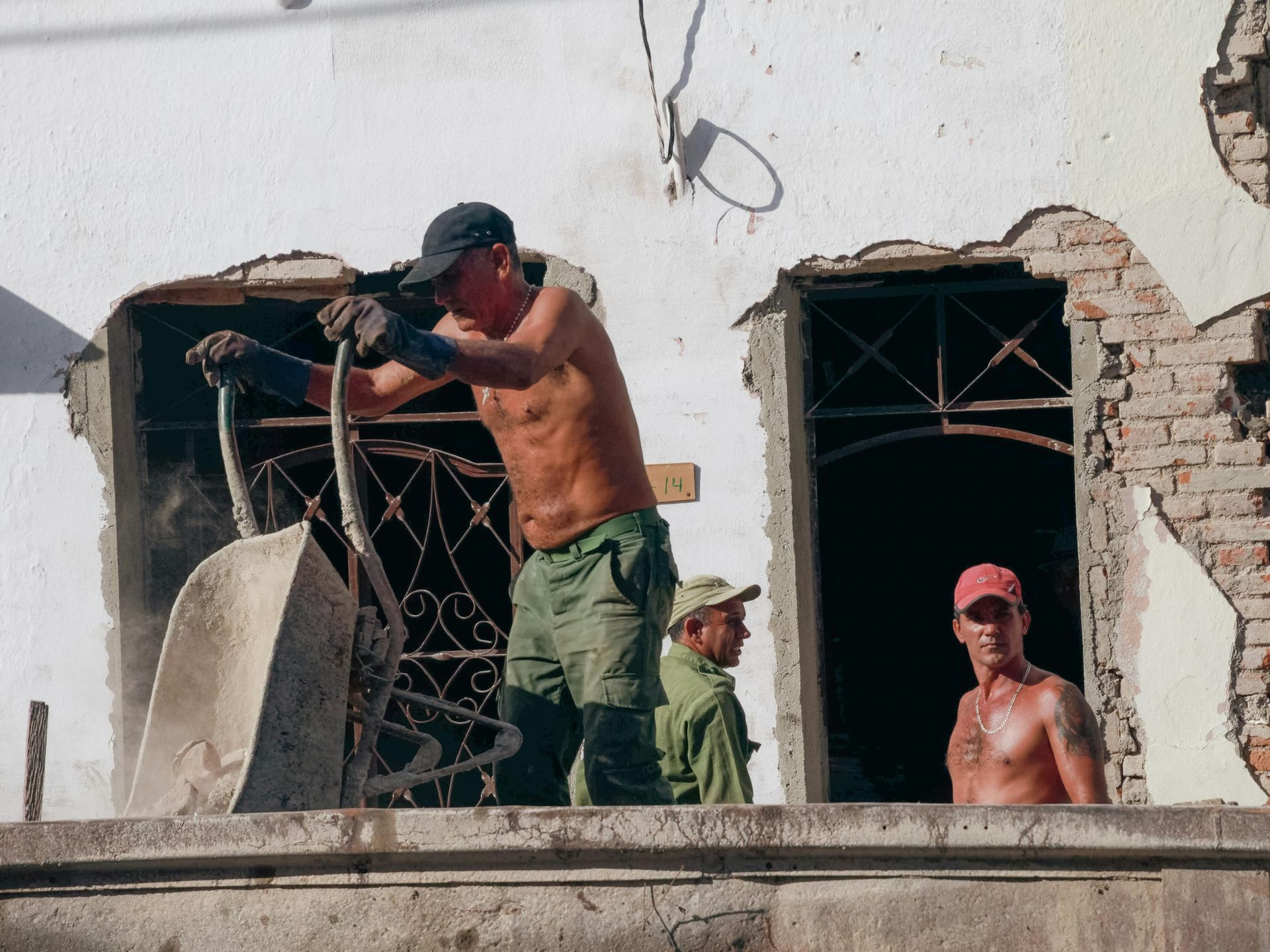 Construction workers removing rubble from a building opening; one shirtless, others visible.