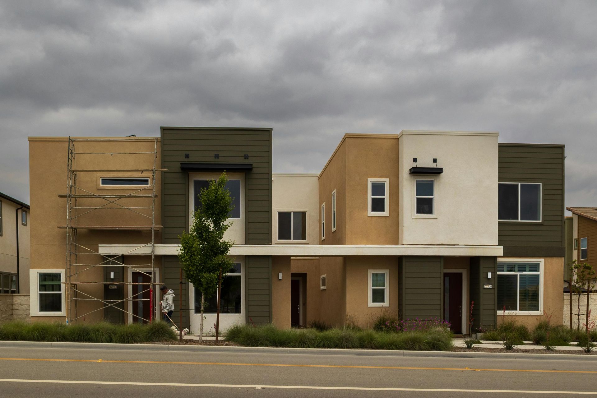 Modern multi-unit building with beige, white, and green facades under a cloudy sky.