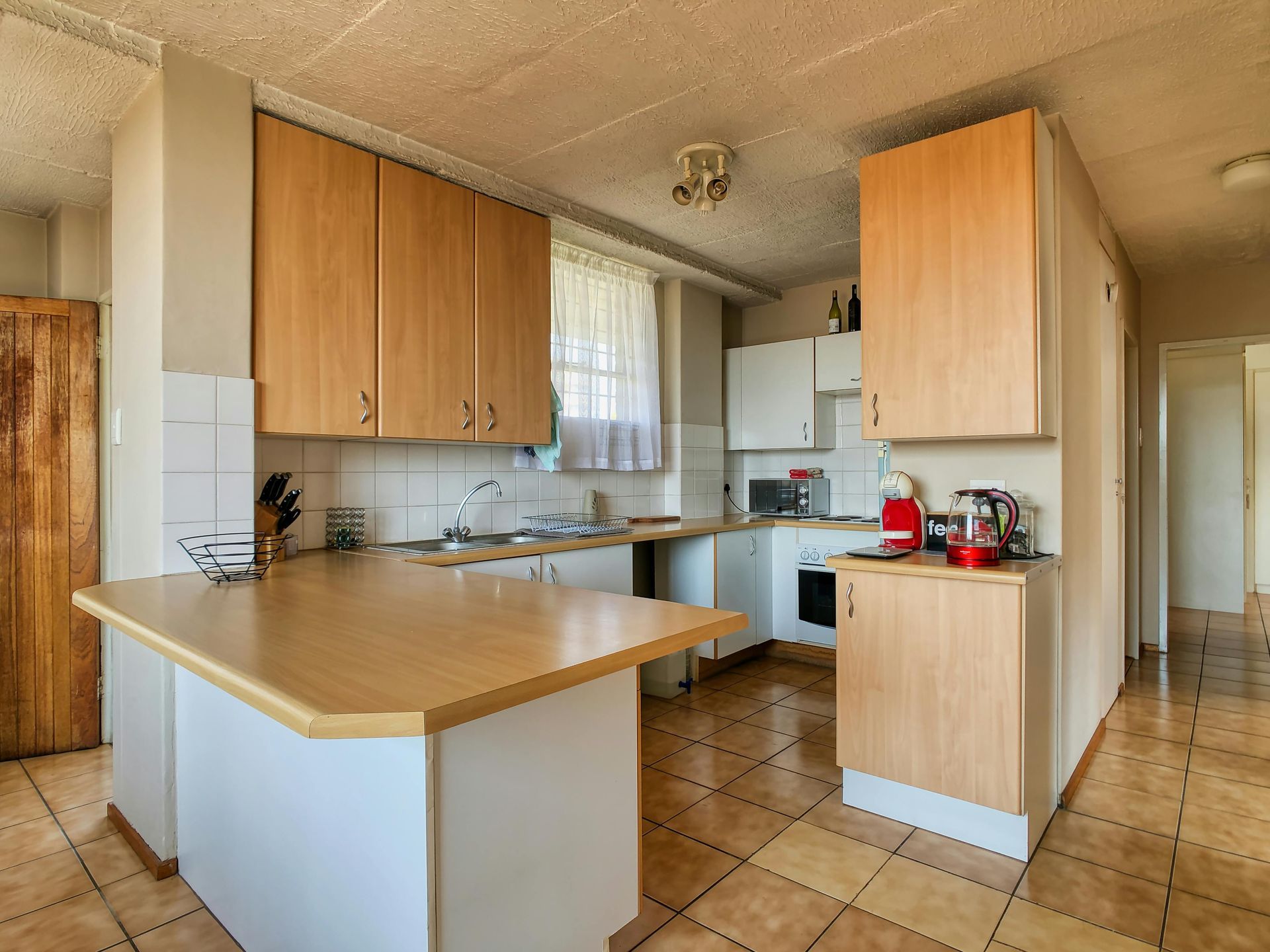 Kitchen with light wood cabinets, white walls, and a tiled floor.