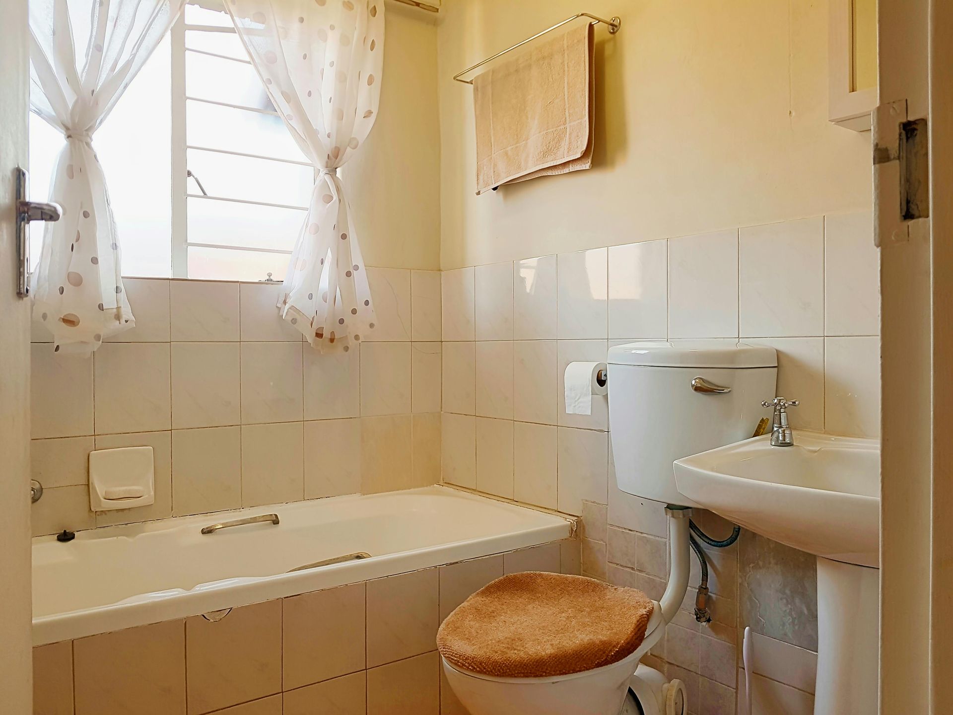 Small bathroom with white tiled walls, a bathtub, and toilet with a closed lid, and sink.