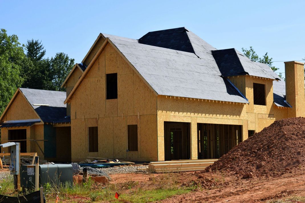 House under construction, wooden frame, gray roof, brown dirt.