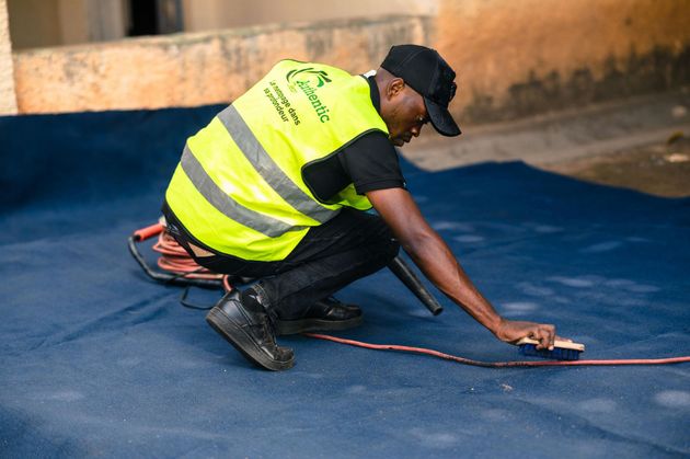 Person in yellow safety vest cleaning a dark blue surface outdoors with a brush.