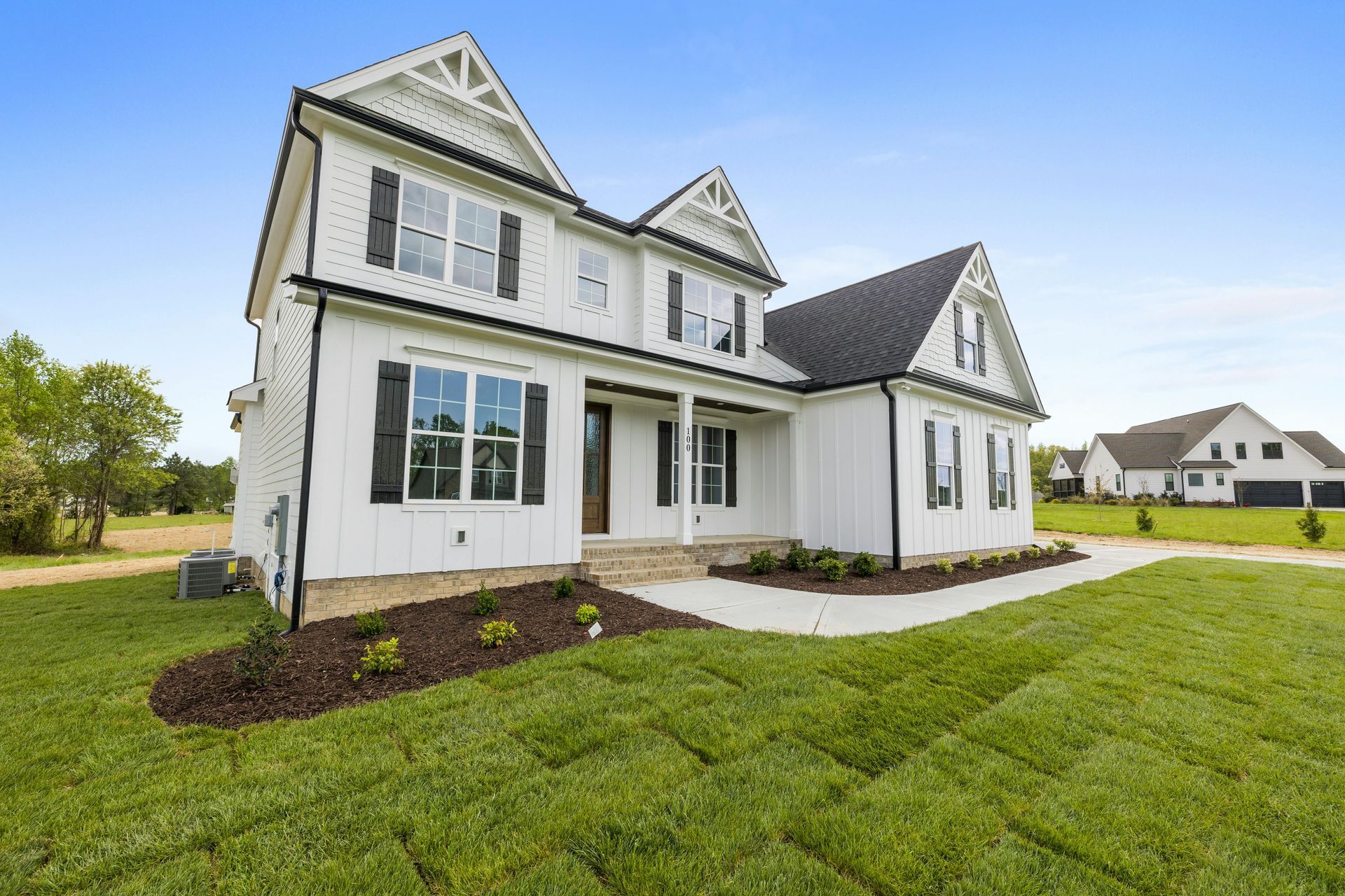 White two-story house with black shutters on green lawn, under blue sky.