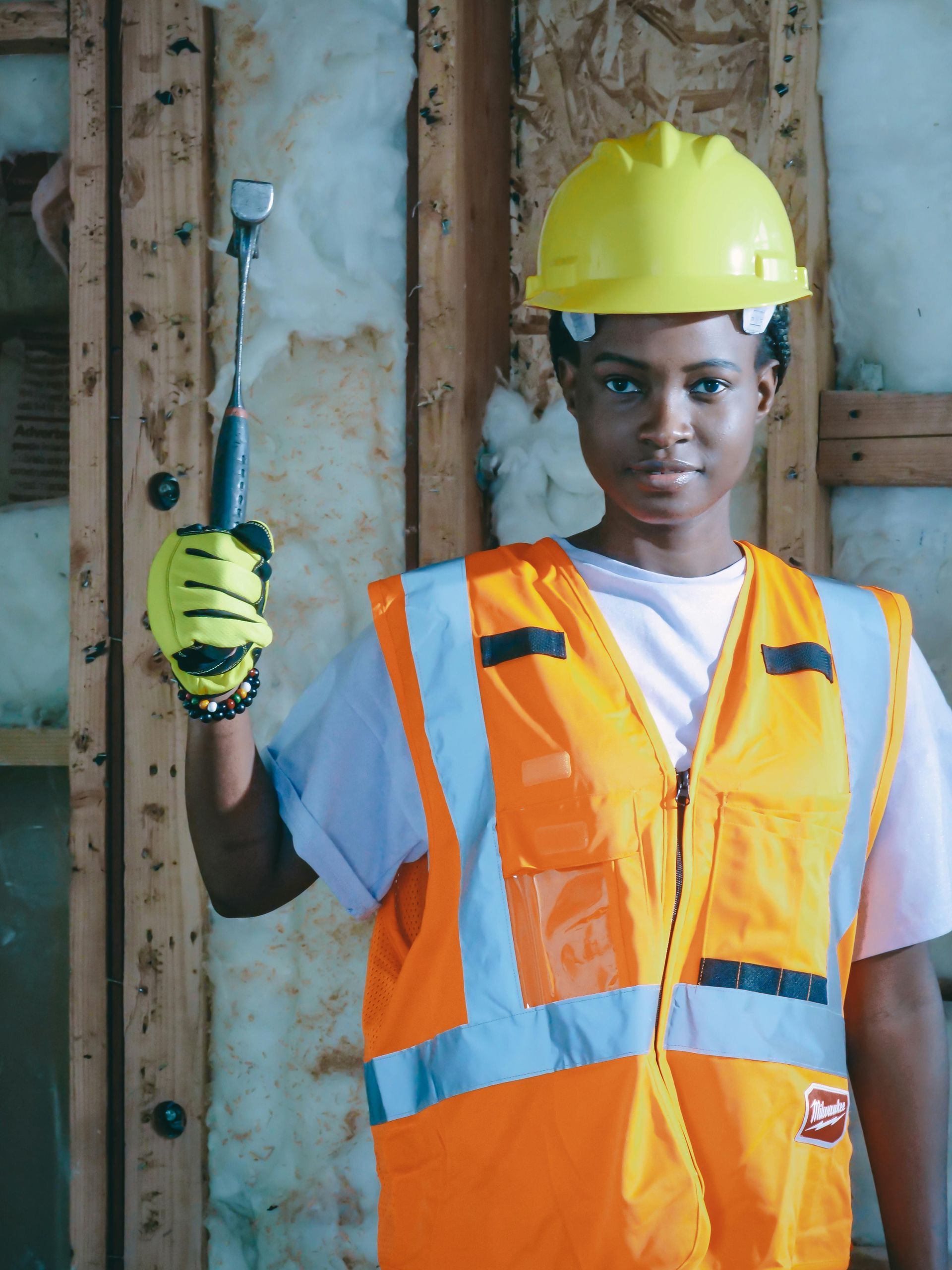 Person in safety gear holding a hammer inside a building under construction.