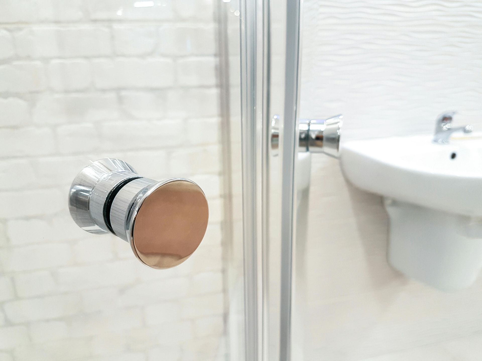 Chrome shower door handle with a white sink in a bathroom.