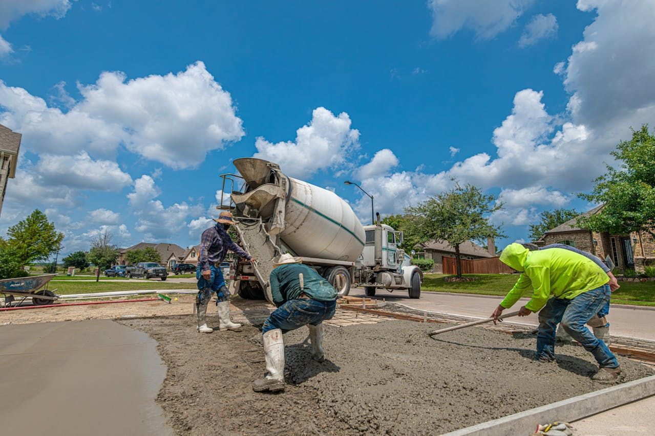 Workers pouring concrete from a mixer truck onto a driveway on a sunny day.