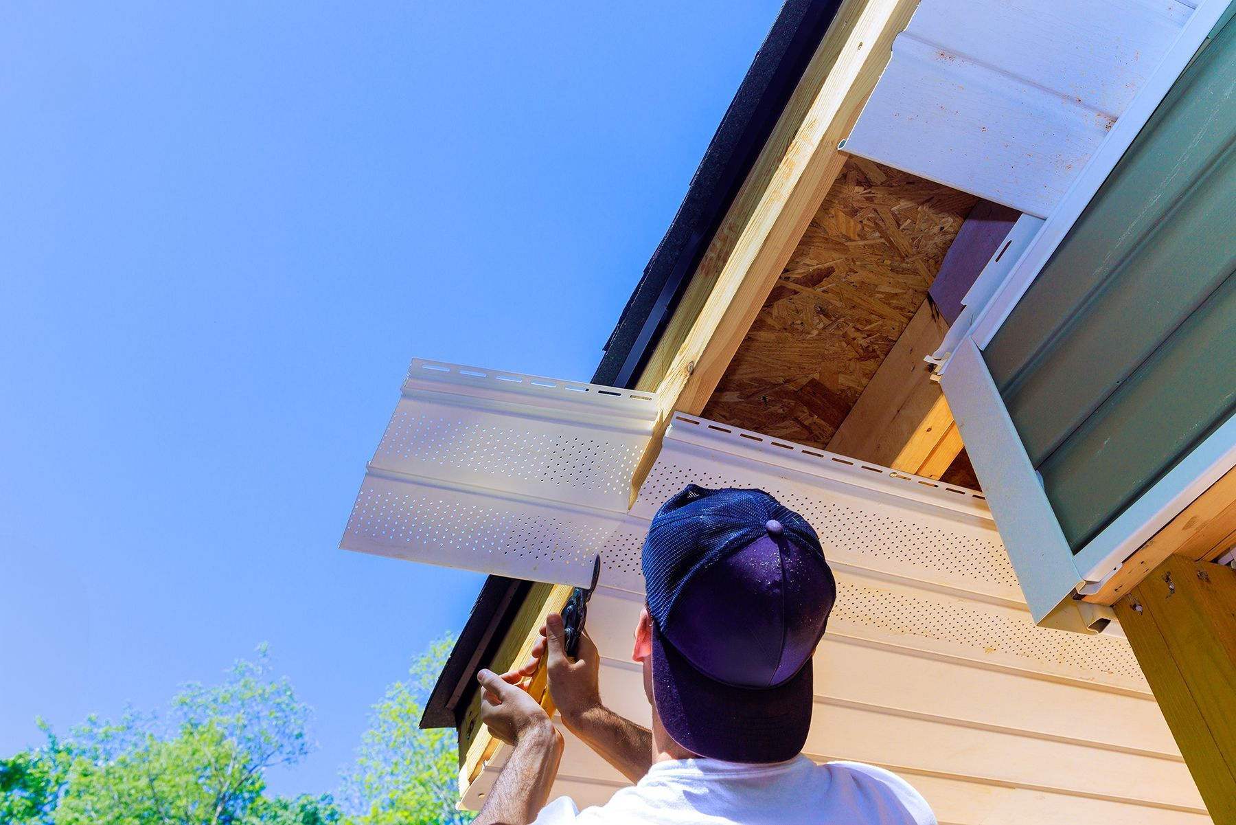 Person installing soffit on a house exterior, under a blue sky.