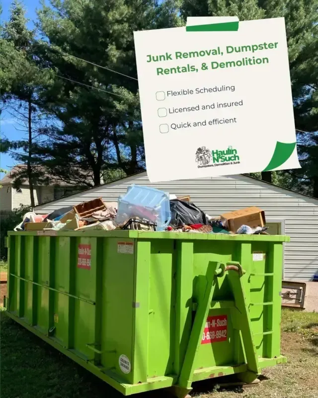 A bright green dumpster filled with junk sits in a yard, with a promotional flyer for Haulin N Such services above it.