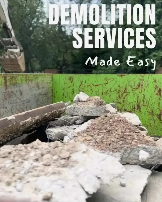 A pile of concrete rubble fills a green industrial dumpster, with an excavator arm visible in the background.