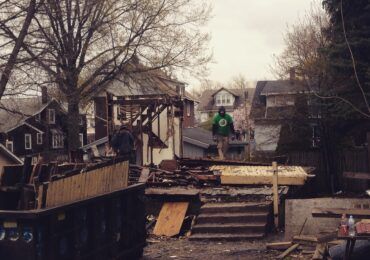 A person in a green shirt stands amidst the demolition debris and wooden framing of a house under construction.