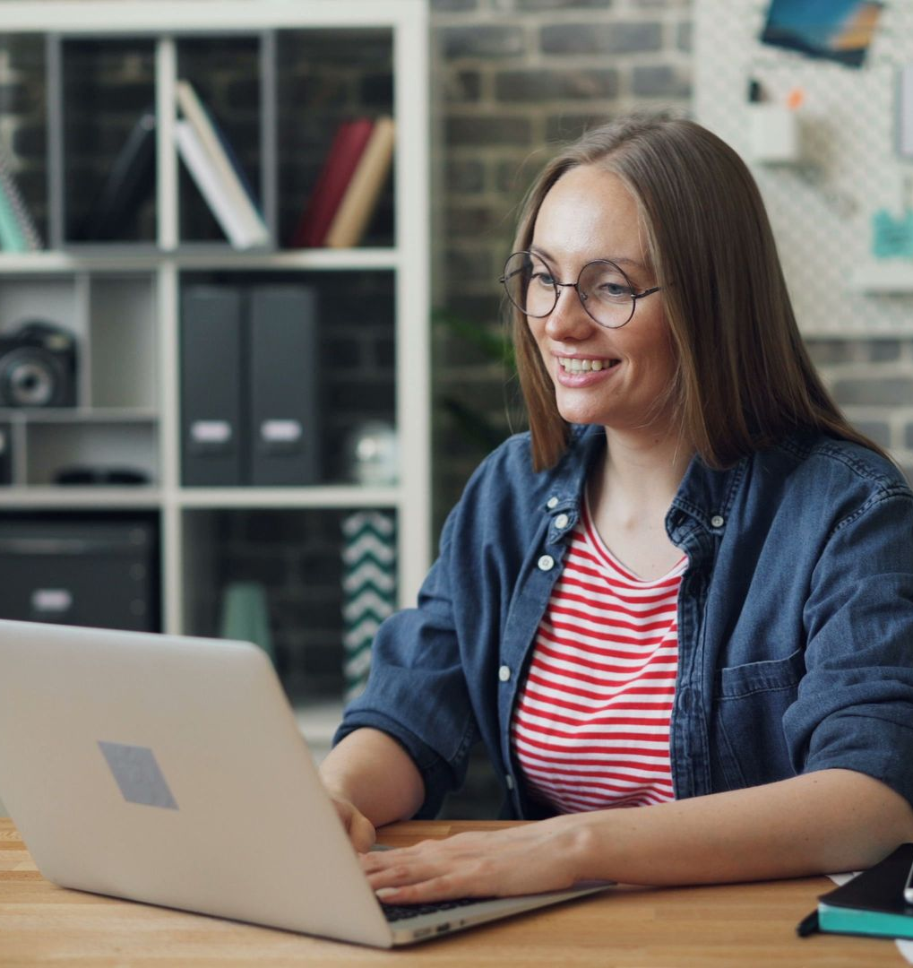 Woman smiling while typing on a laptop at a desk in an office