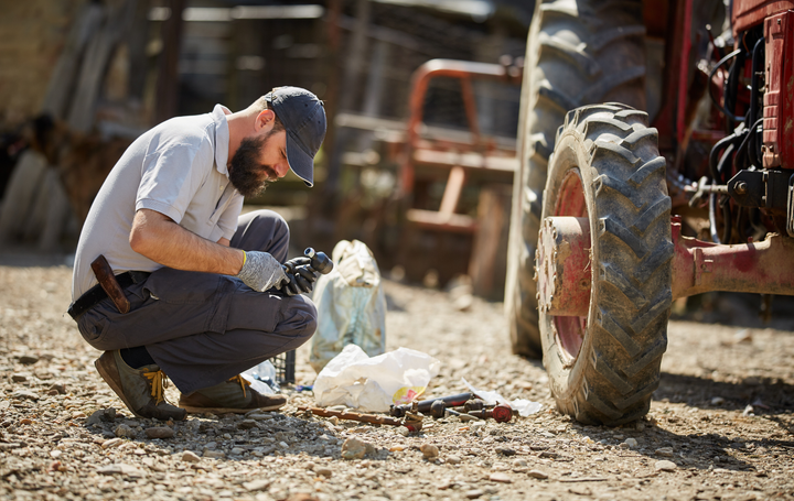 A man is working on a tractor in a dirt field.