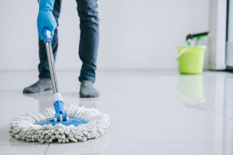 Person mopping a white tile floor with a blue mop and gloved hands
