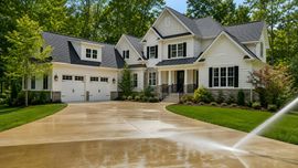 Large cream-colored suburban house with a three-car garage and wet driveway, being watered by sprinklers.