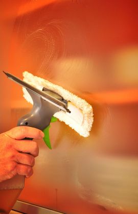 Hand cleaning a glossy orange wall with a squeegee and white cloth