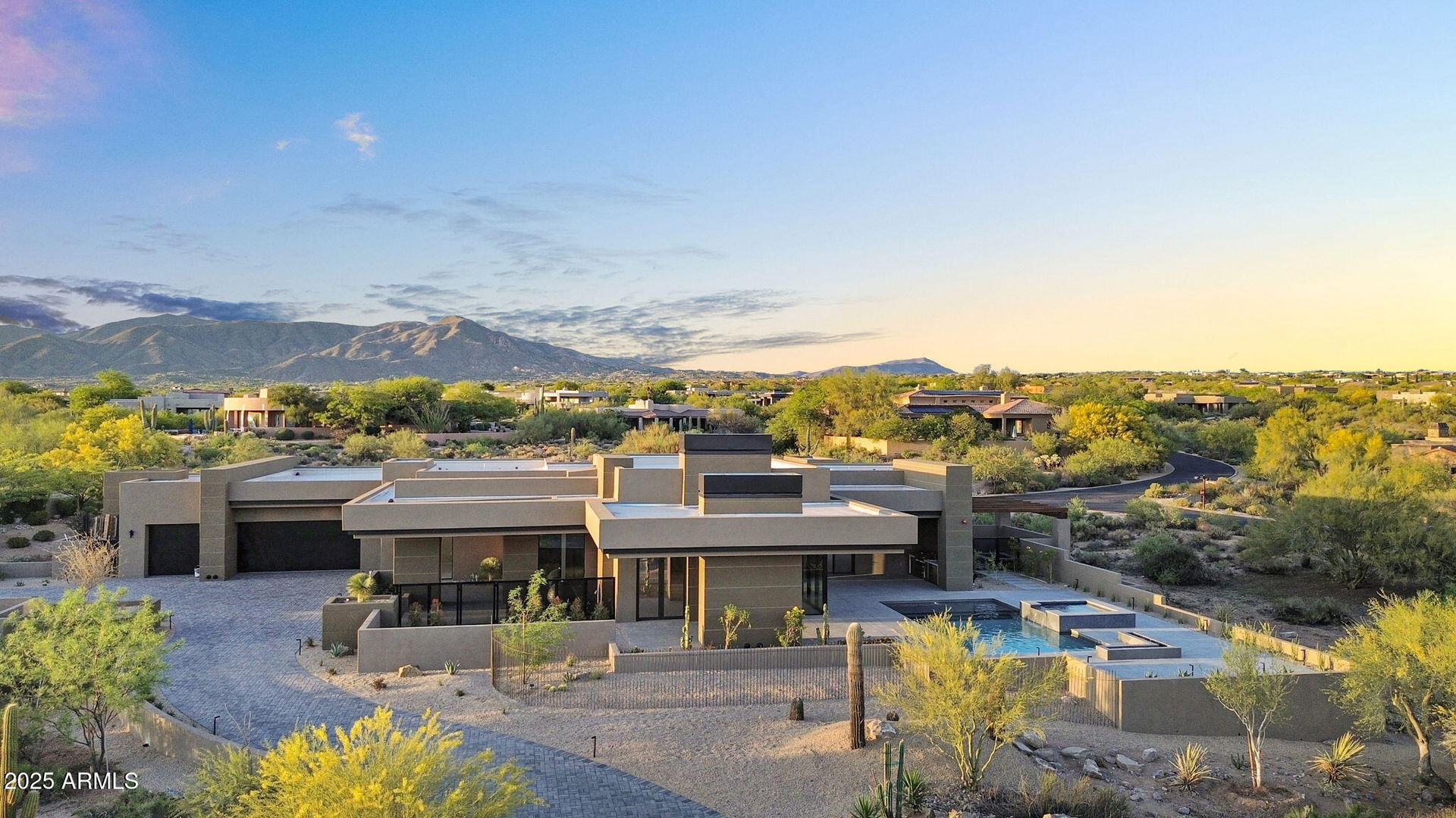 An aerial view of a large house in the desert with mountains in the background.