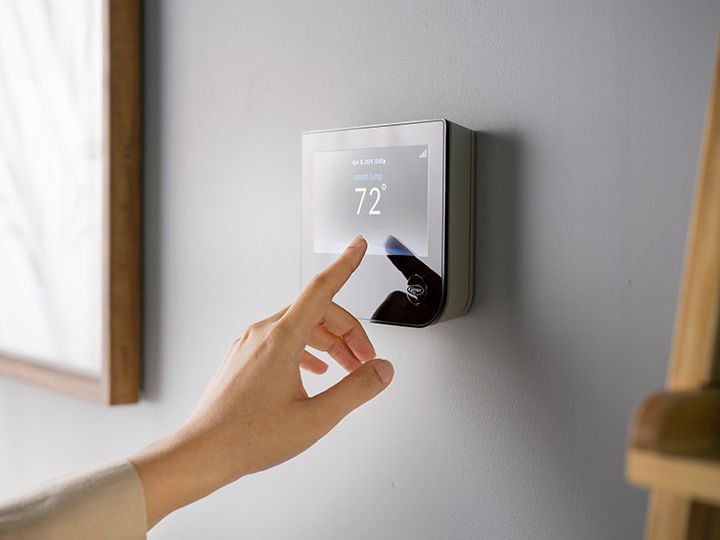 Round black smart thermostat on a wall, displaying 72° with a blue digital interface in a bright room.
