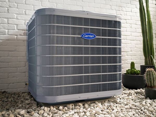 Outdoor gray air conditioner unit beside a wall, surrounded by landscaping and grass