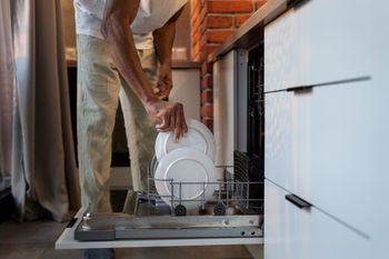 Person loading a white plate into an open dishwasher in a kitchen