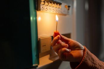 Hand lighting a match beside a wall-mounted gas meter in dim light