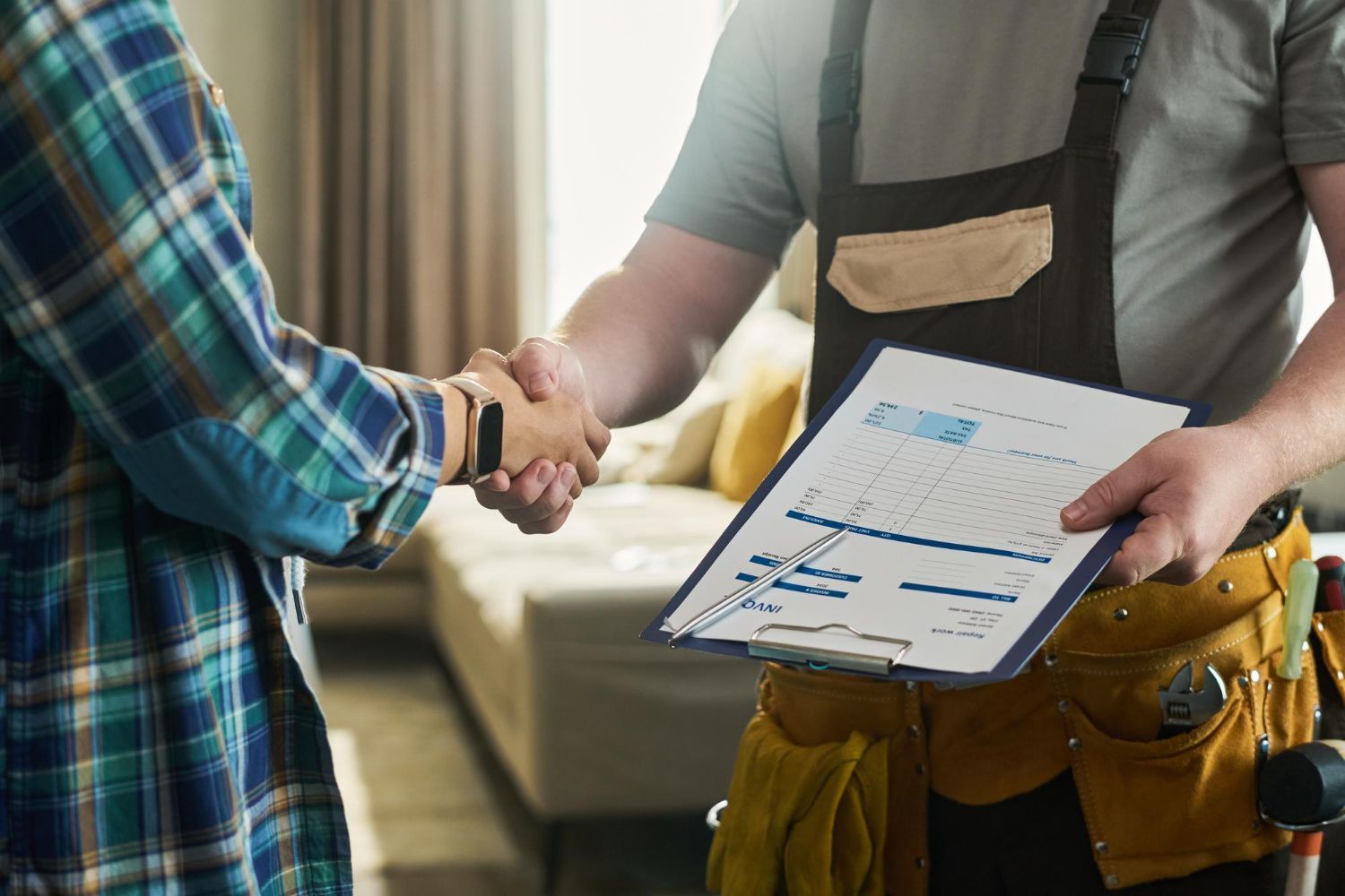 Home inspector shaking hands with a homeowner while holding a clipboard in a living room