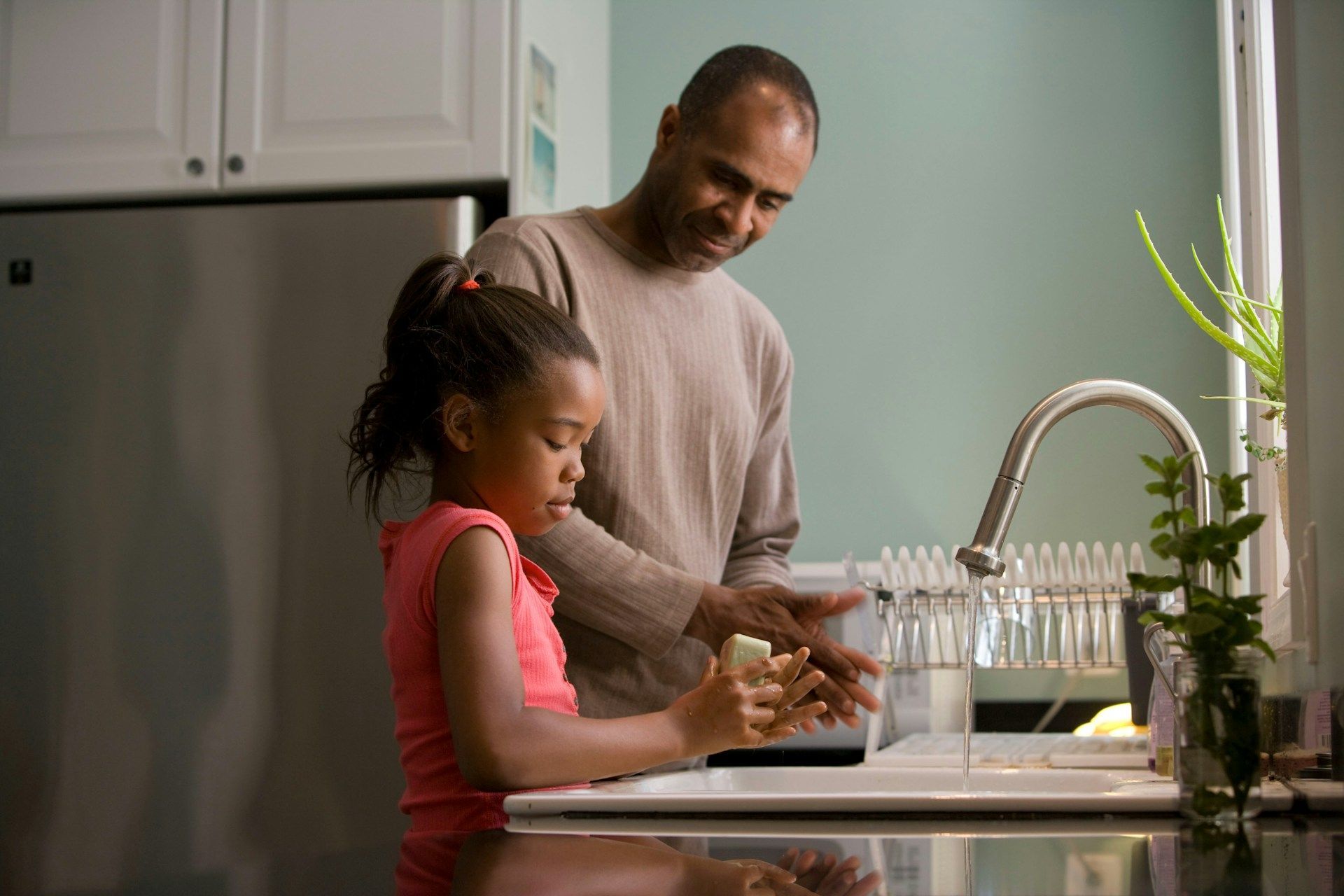 Adult and child washing dishes together in a kitchen beside a sink and dish rack.
