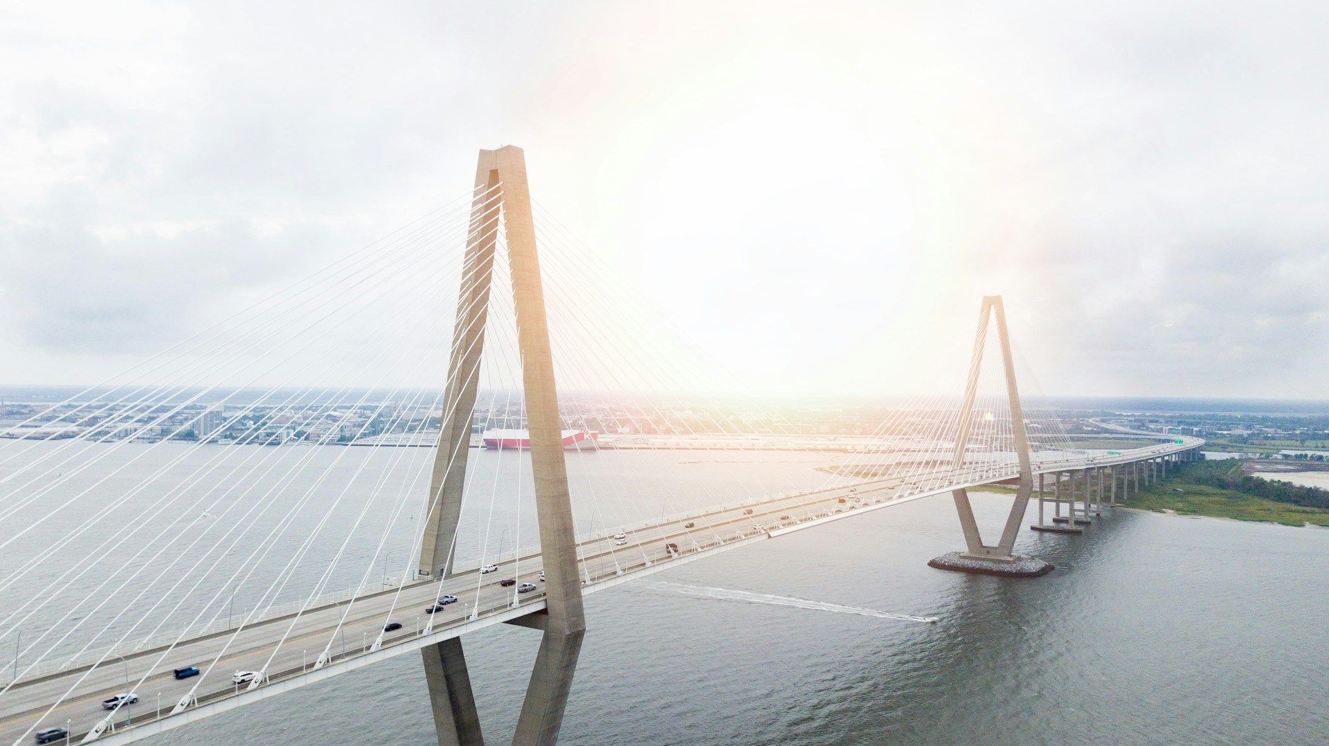 Long cable-stayed bridge over water at sunset with two tall towers and a distant shoreline