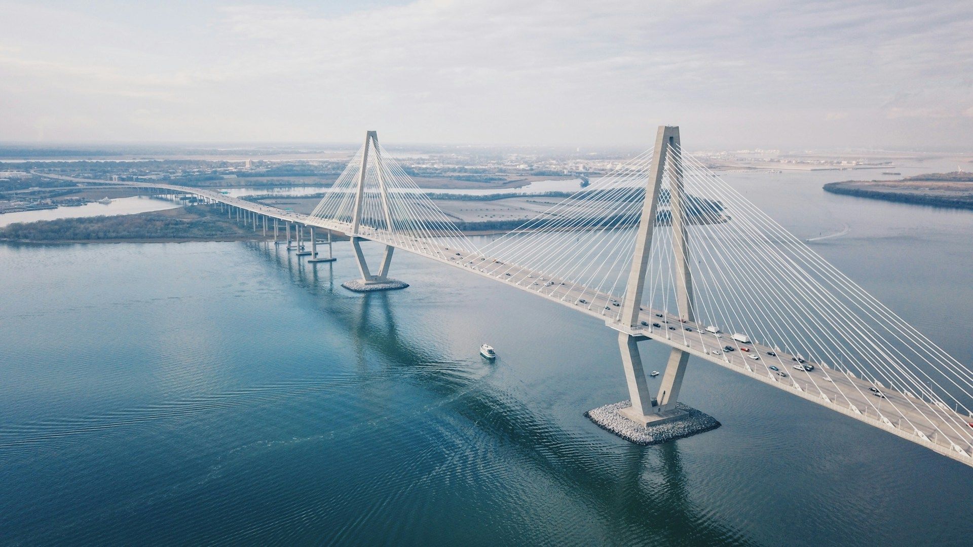 Aerial view of a cable-stayed bridge spanning blue water with ships nearby.