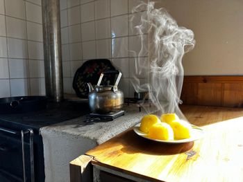 Steaming teapot on a stove beside a plate of lemon wedges in a sunlit kitchen