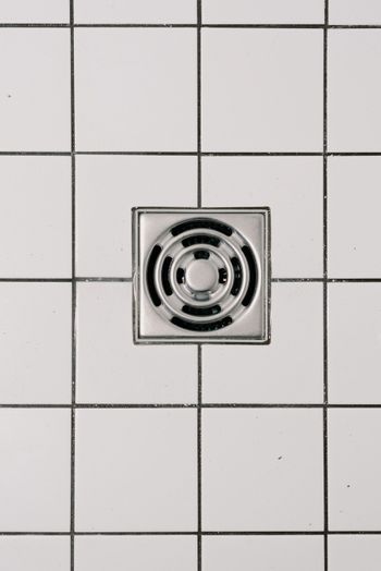 Square metal drain cover set in white tiled floor