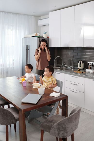 Three people in a bright kitchen, one taking a photo while two sit at a dining table with laptops and cups.
