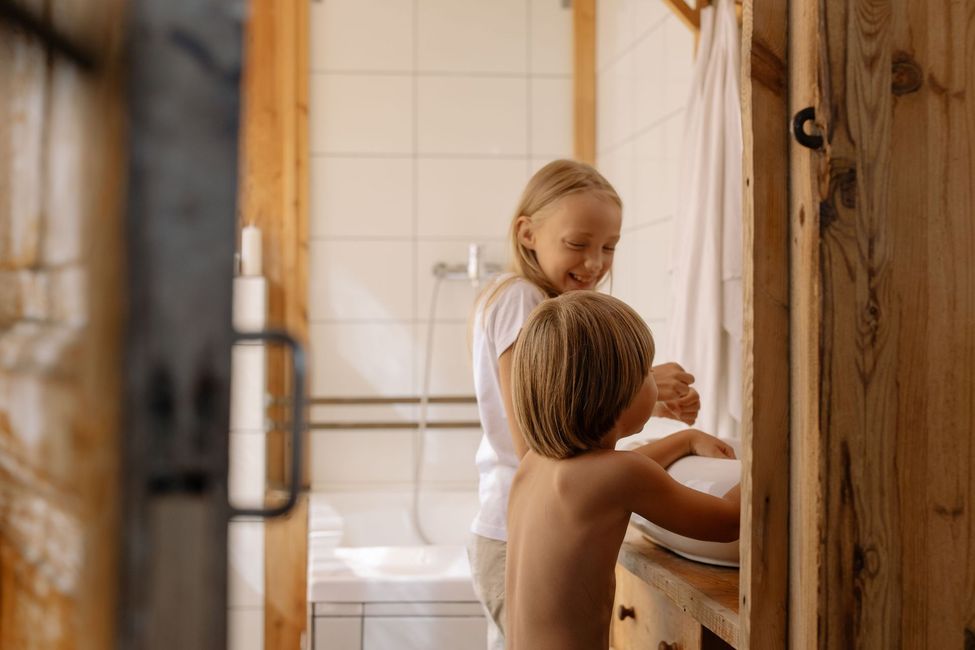 Two children washing hands at a bathroom sink beside a shower curtain