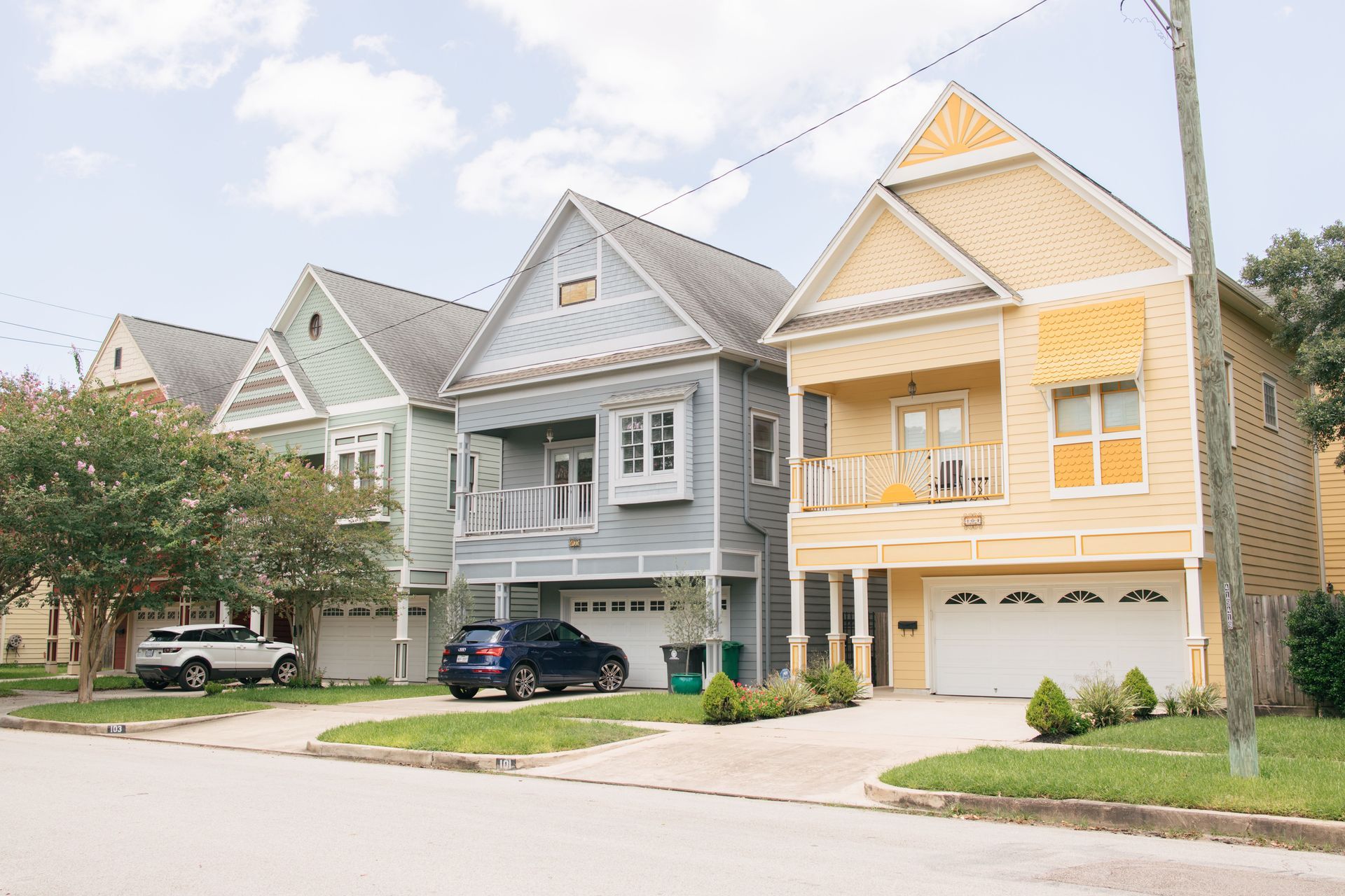 Row of pastel suburban townhouses with parked cars and a tree-lined street