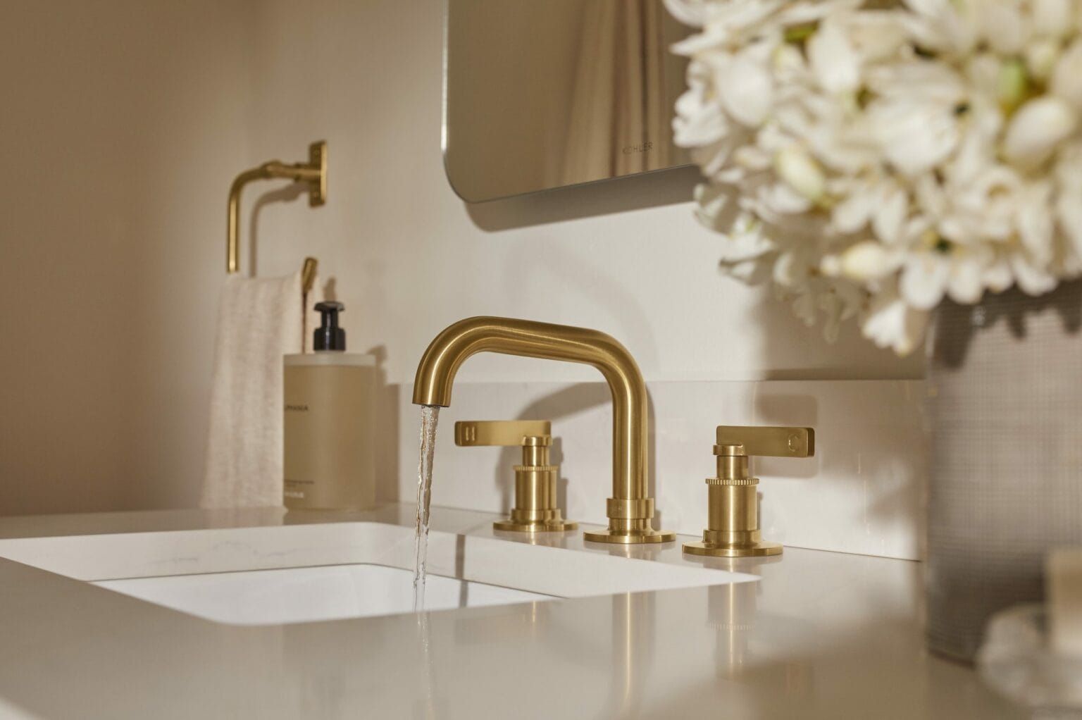 A bathroom sink with gold faucets and a vase of flowers.