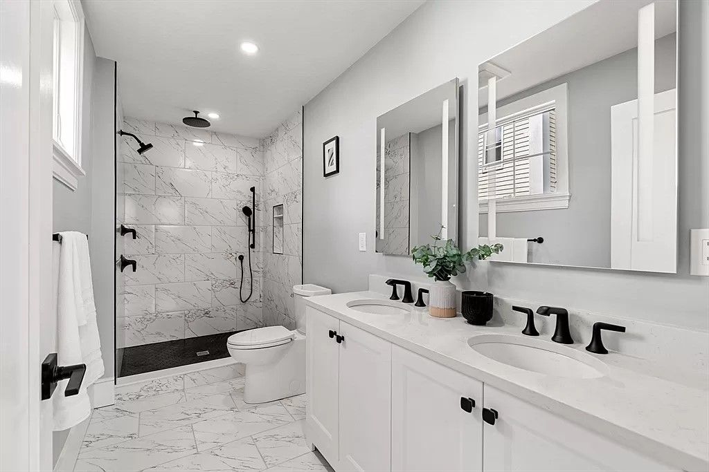 A bathroom with two sinks , a toilet , and a walk in shower.