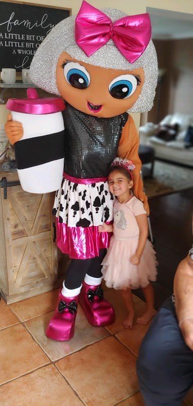 A person in a doll costume with a child, holding a coffee cup, standing on tiled floor.