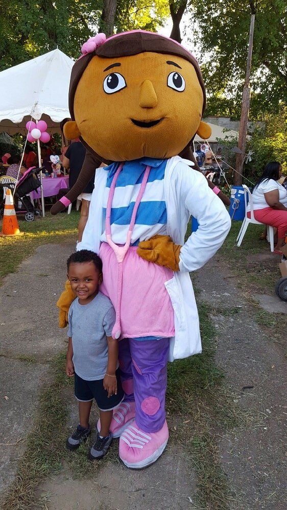 Boy posing with Doc McStuffins mascot in outdoor setting.